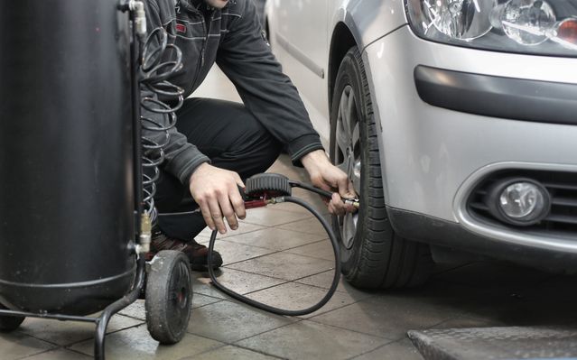 Osoba naduvava gumu automobila pomoću kompresora