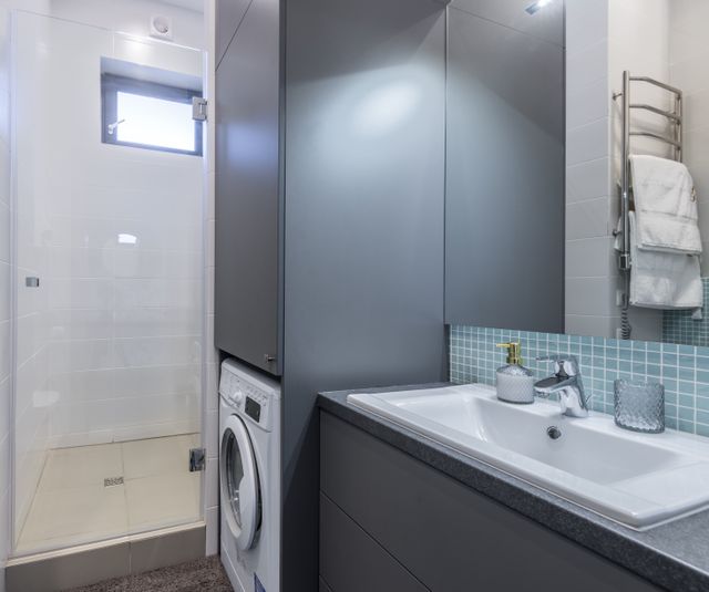 Lavabo sa hromiranom slavinom, sivim ormarićem i veš mašinom pored tuša